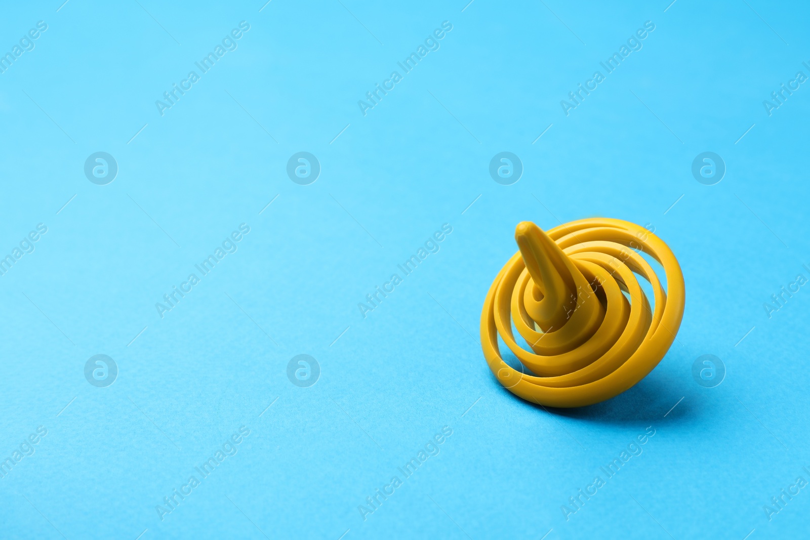 Photo of One yellow spinning top on light blue background, space for text
