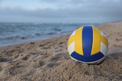 Photo of Colorful volleyball ball on sand near sea. Space for text