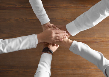 Photo of People holding hands together over wooden background, top view. Unity concept