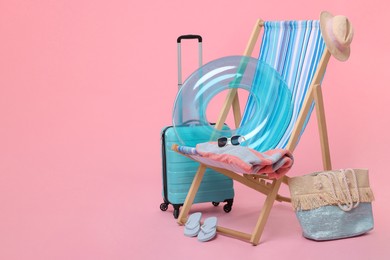 Deck chair, suitcase and beach accessories on pink background, space for text. Summer vacation