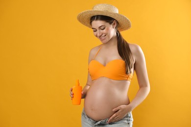 Young pregnant woman with sun protection spray on yellow background. space for text