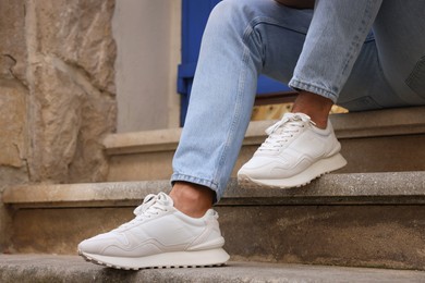 Photo of Man wearing pair of stylish sneakers on stairs outdoors, closeup