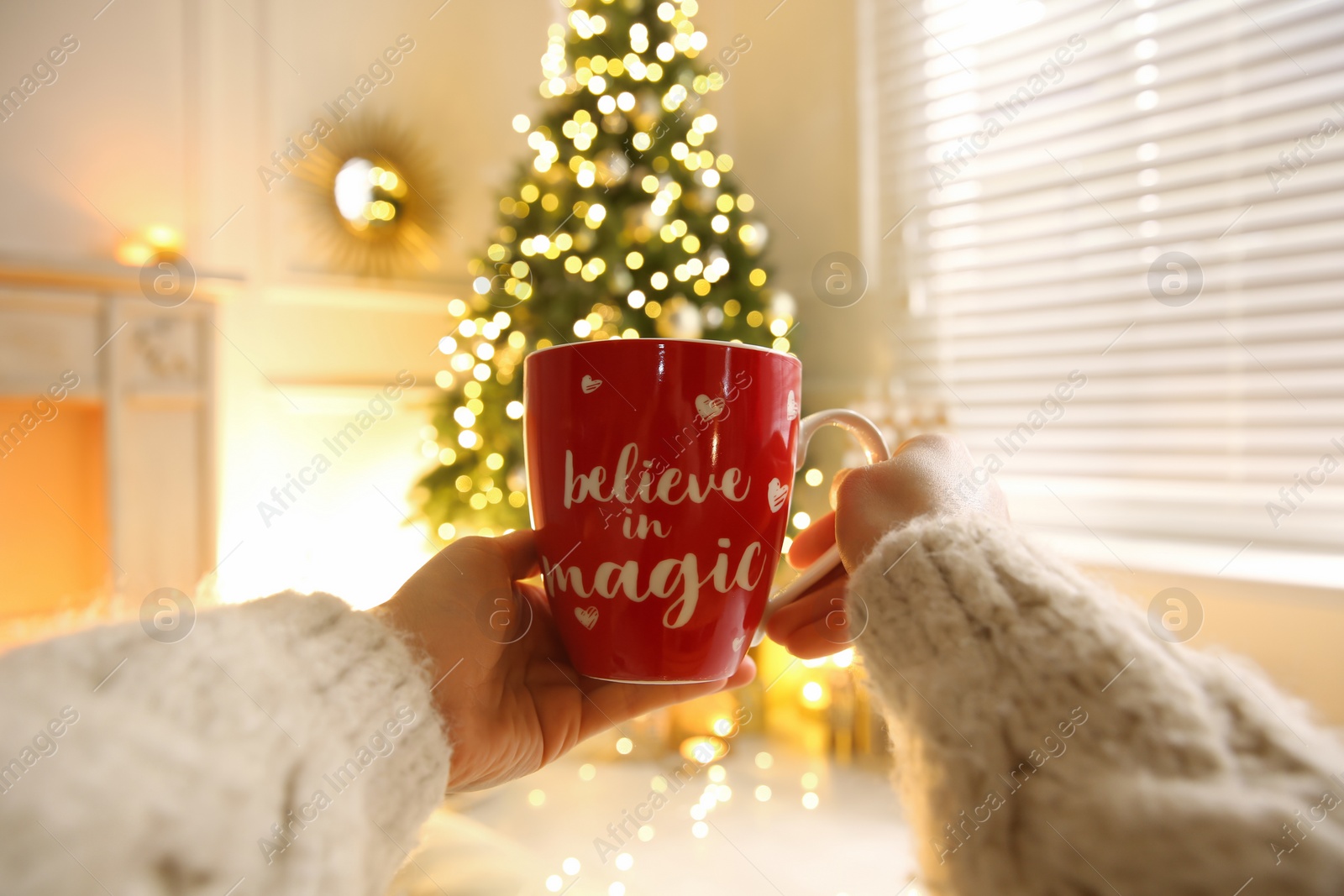 Photo of Woman with cup of drink and blurred Christmas tree on background, closeup