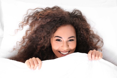 Young African-American woman lying under blanket, top view. Bedtime