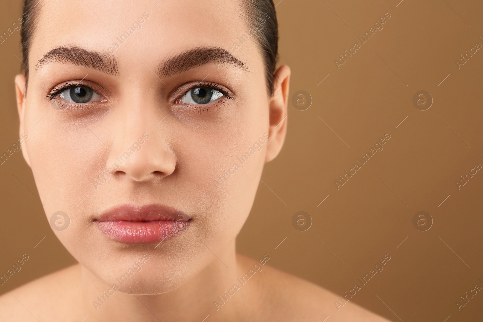 Photo of Young woman with perfect eyebrows on brown background, closeup. Space for text