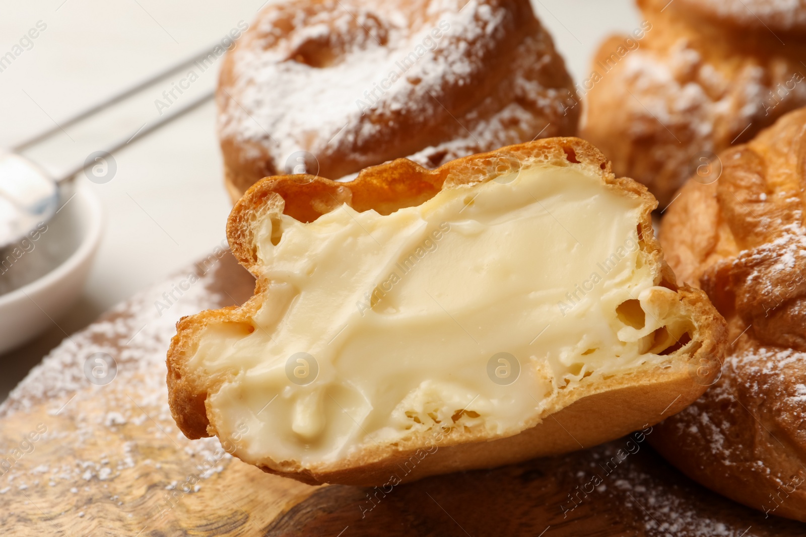 Photo of Delicious profiteroles with cream filling inside on wooden table, closeup