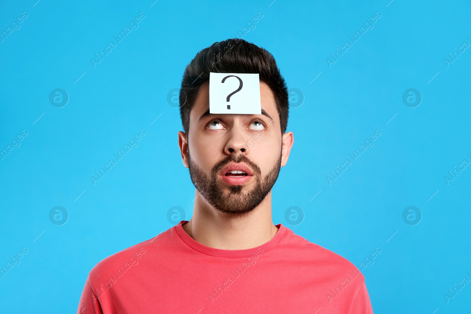 Photo of Emotional young man with question mark sticker on forehead against light blue background