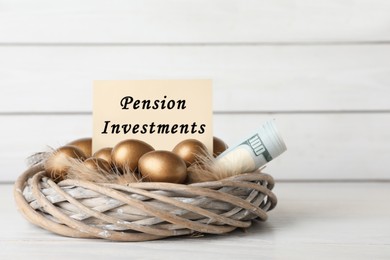 Photo of Many golden eggs, money and card with phrase Pension Investments on table near white wooden wall