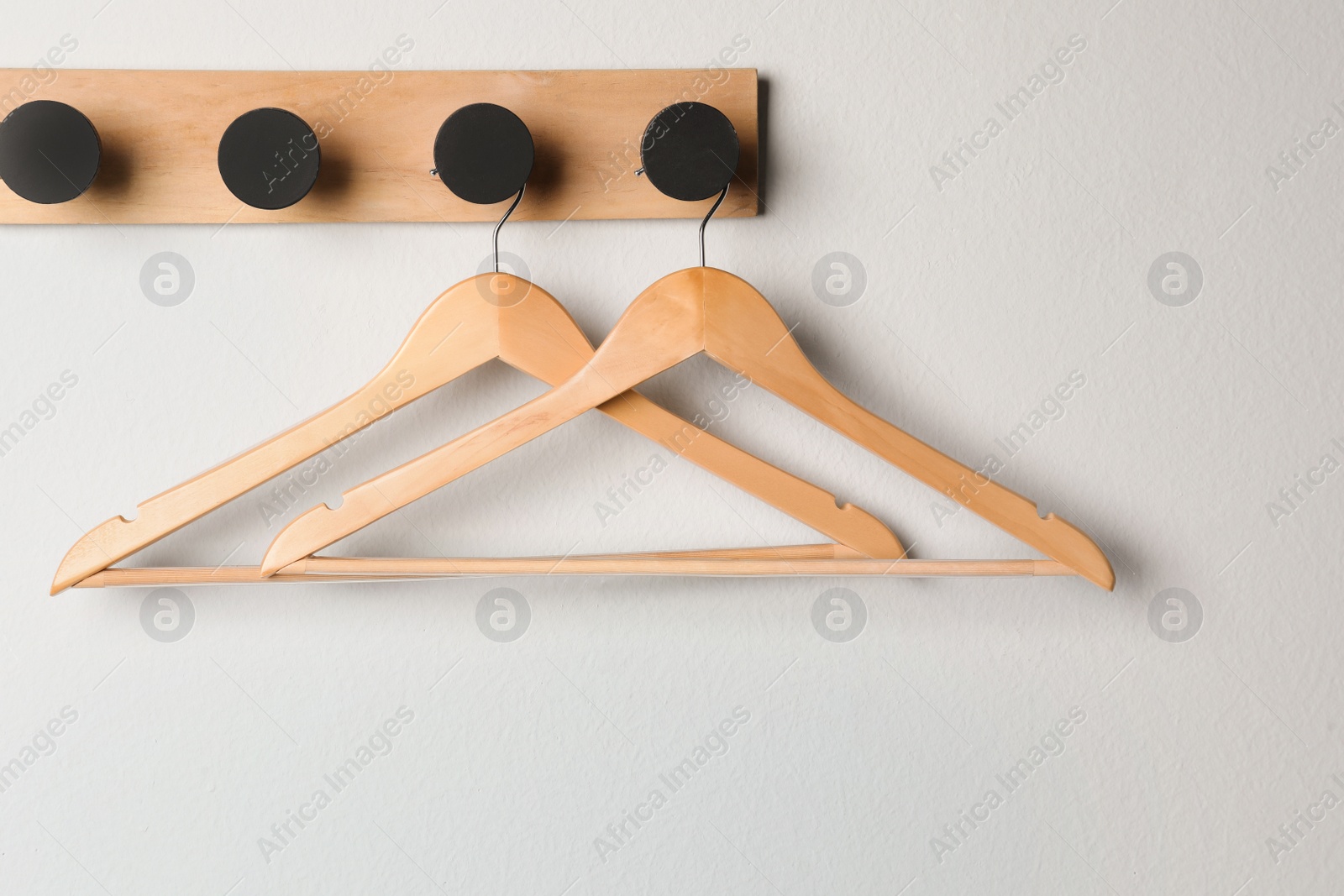 Photo of Rack with empty wooden clothes hangers on white wall