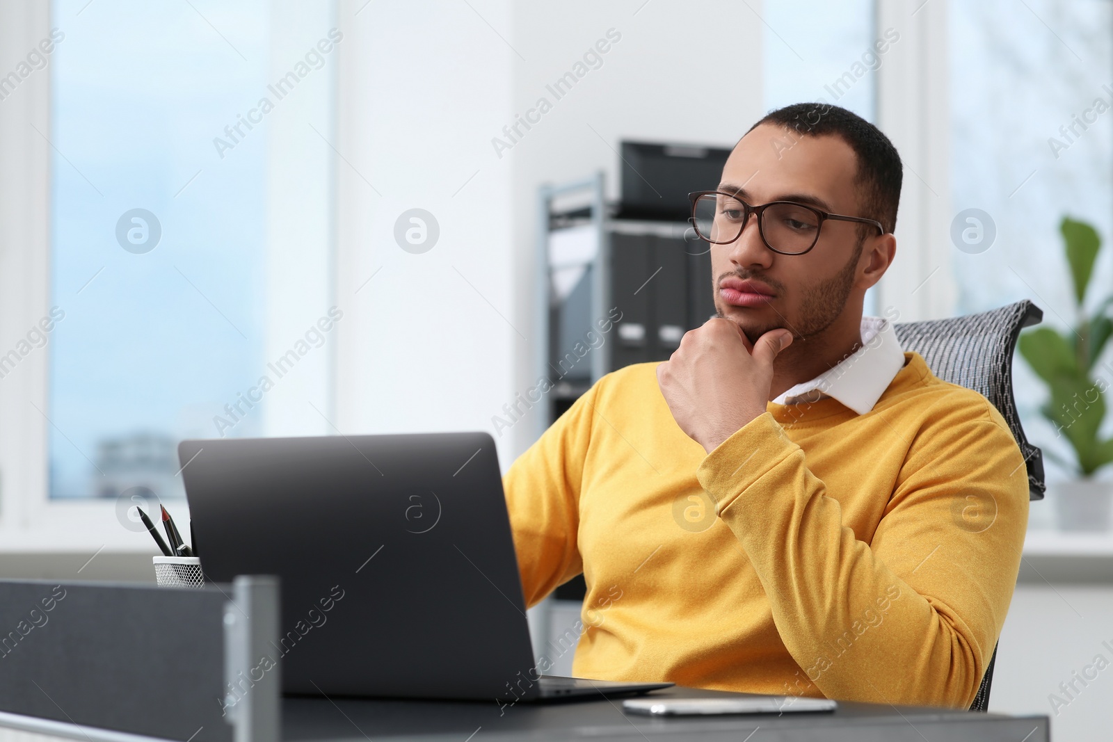 Photo of Young man working on laptop at table in office