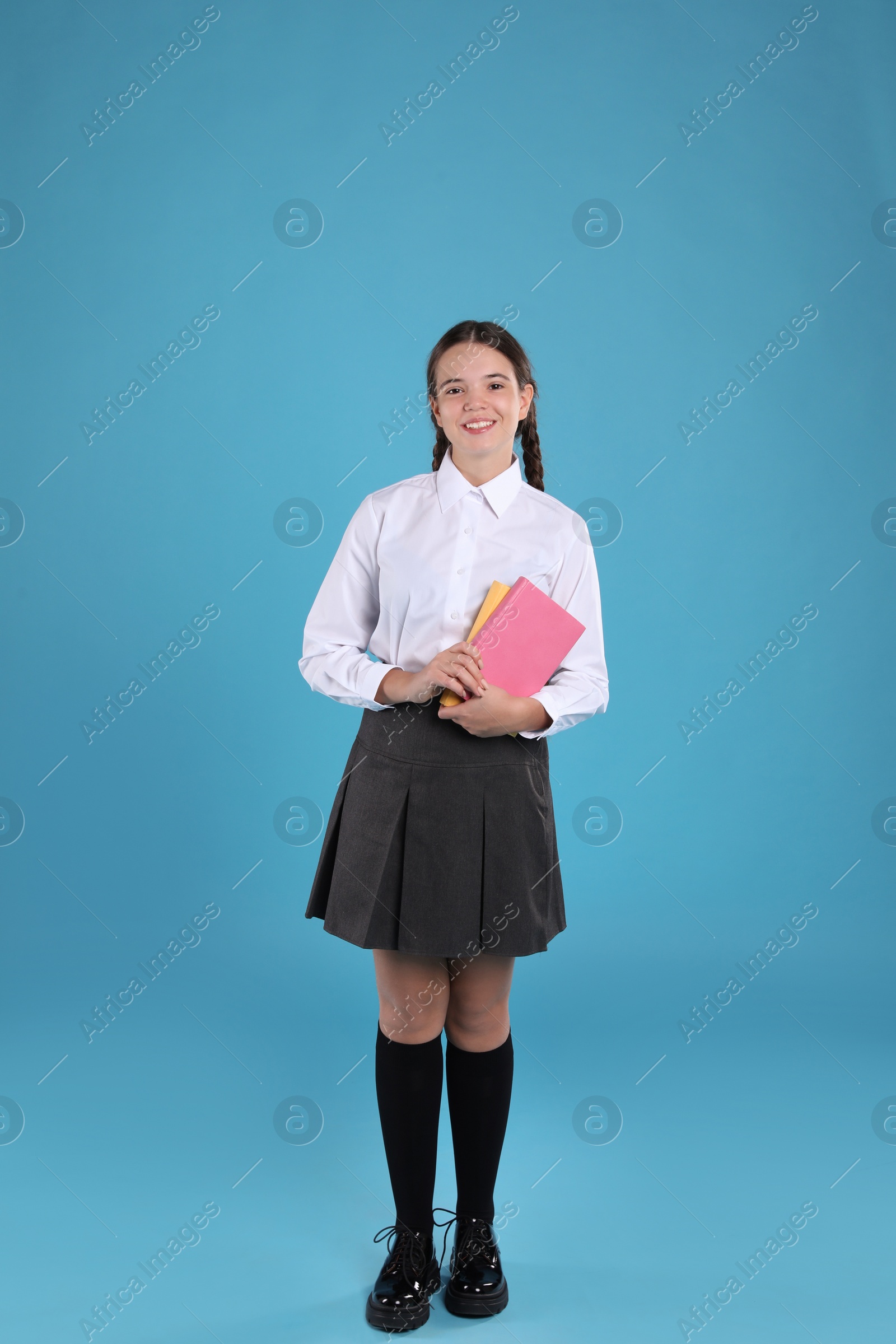 Photo of Teenage girl in school uniform with books on light blue background