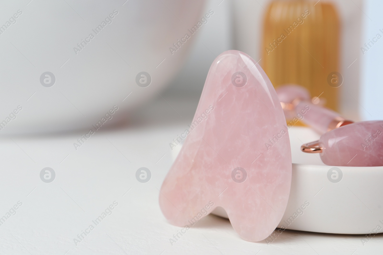 Photo of Rose quartz gua sha tool and natural face roller on white table, closeup. Space for text