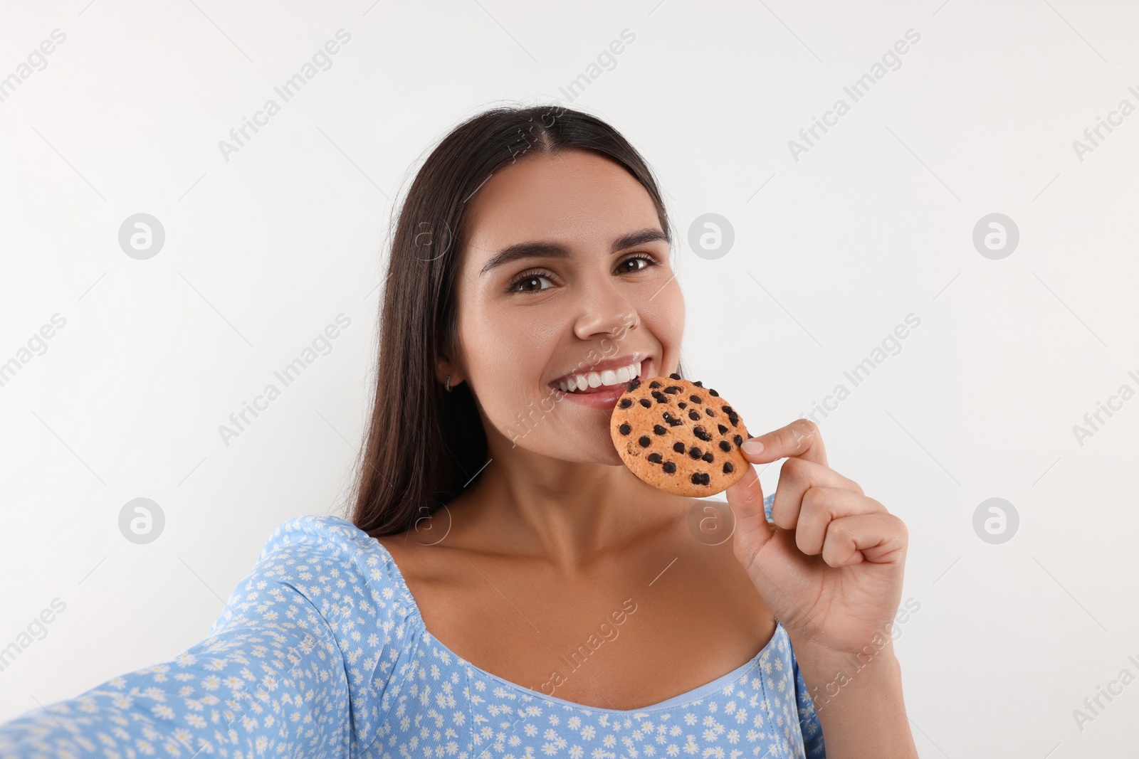 Photo of Young woman with chocolate chip cookie taking selfie on white background