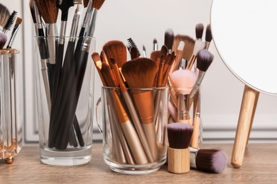 Photo of Set of professional makeup brushes and mirror on wooden table near white wall