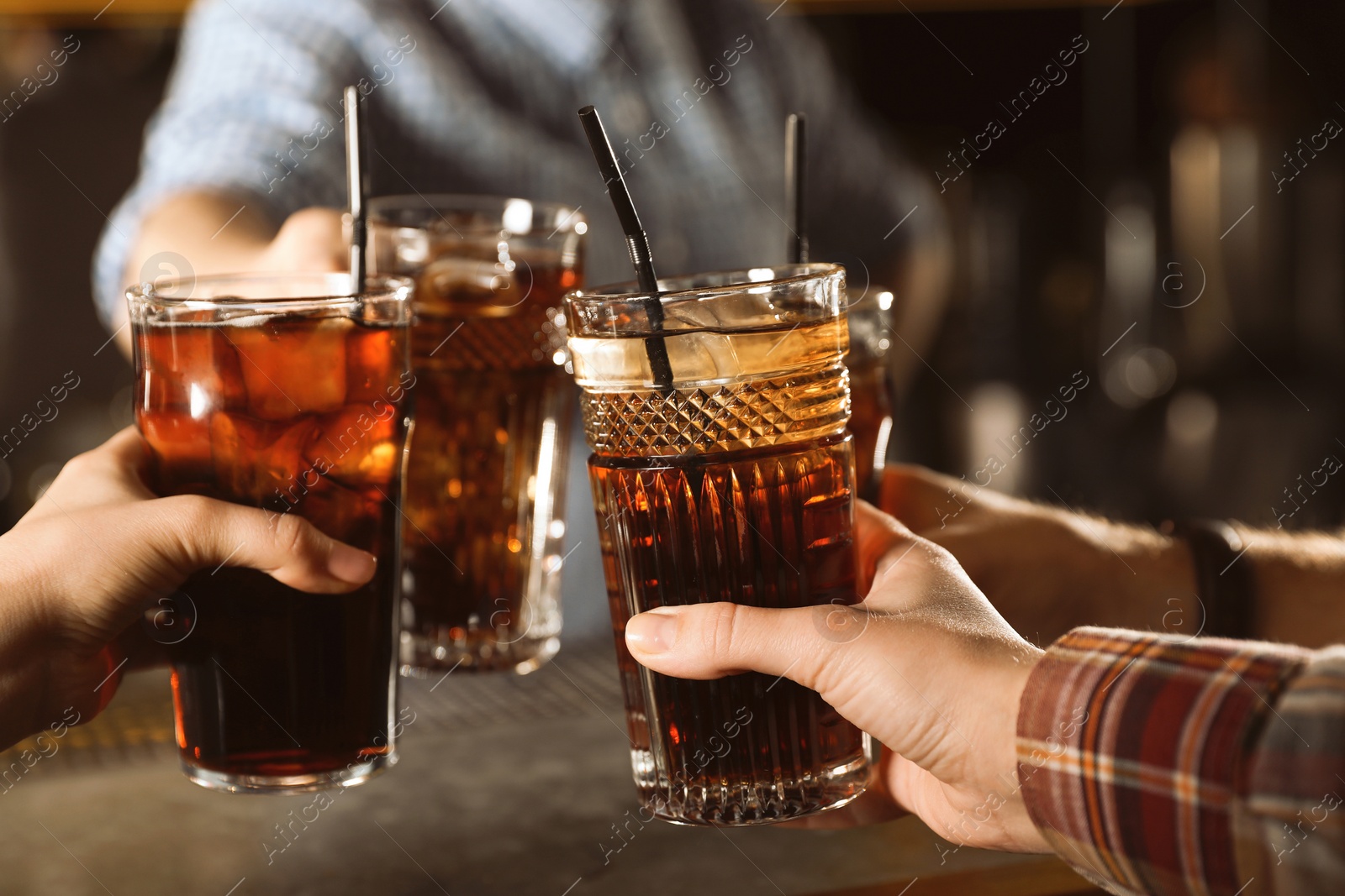 Photo of Group of friends clinking glasses with cola at table indoors, closeup