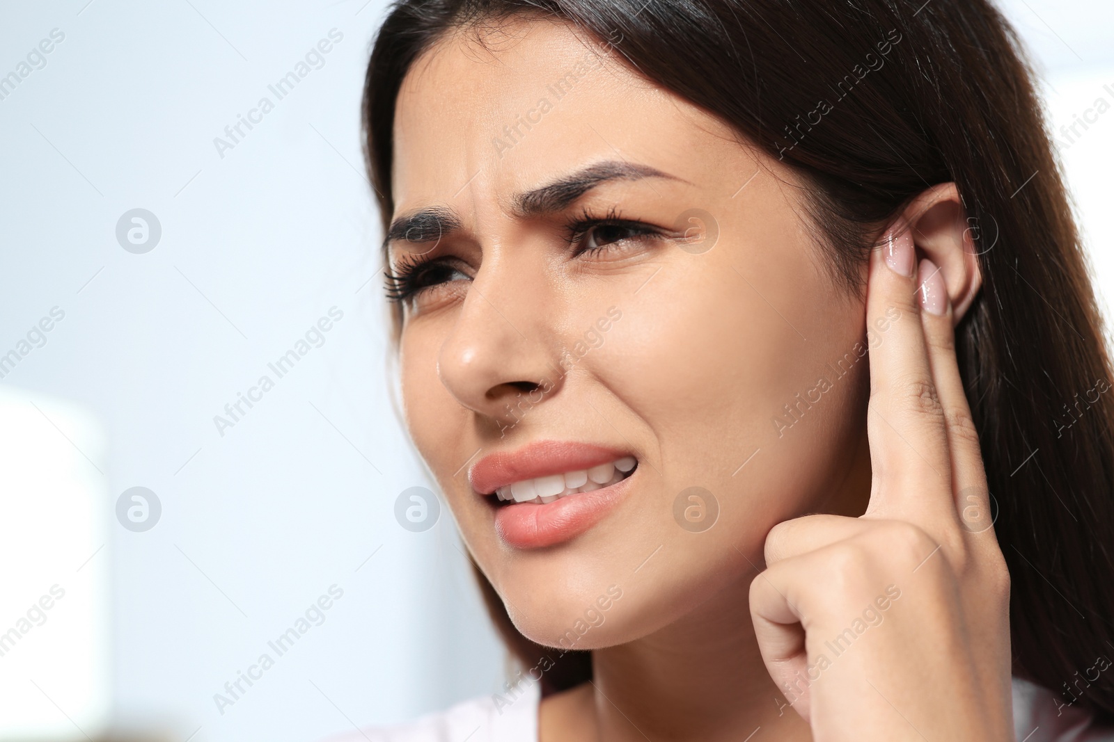 Photo of Young woman suffering from ear pain on blurred background, closeup. Space for text