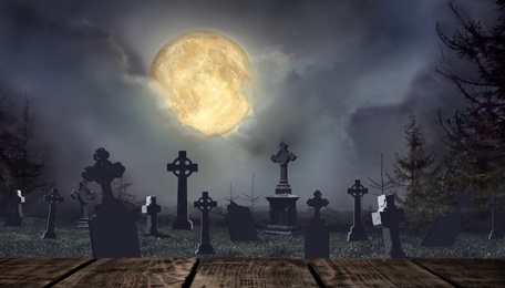 Image of Wooden surface and moonlit graveyard with old creepy headstones on Halloween