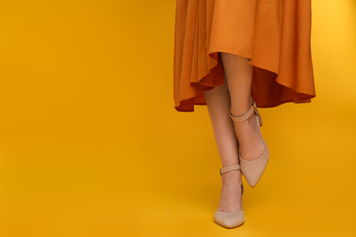 Photo of Woman wearing stylish shoes on yellow background, closeup. Space for text