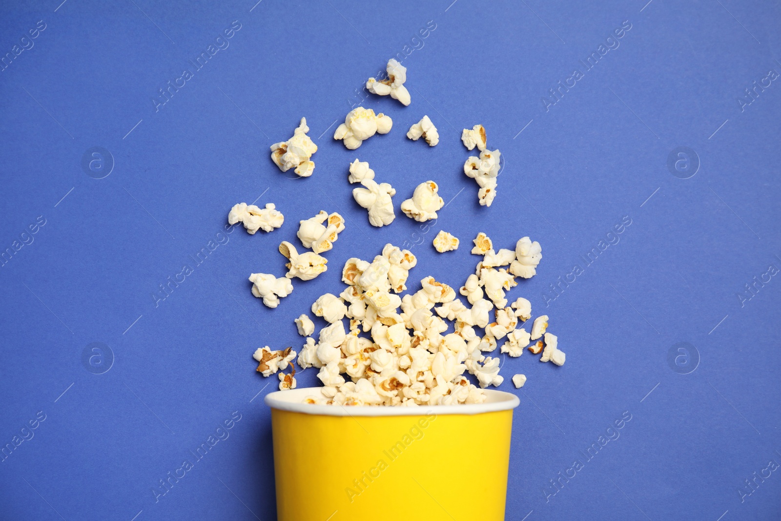 Photo of Paper cup with tasty fresh popcorn on color background, top view