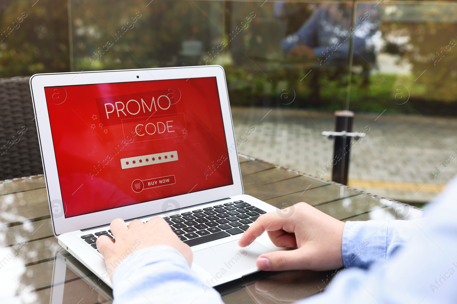 Photo of Man with laptop activating promo code at wooden table outdoors, closeup