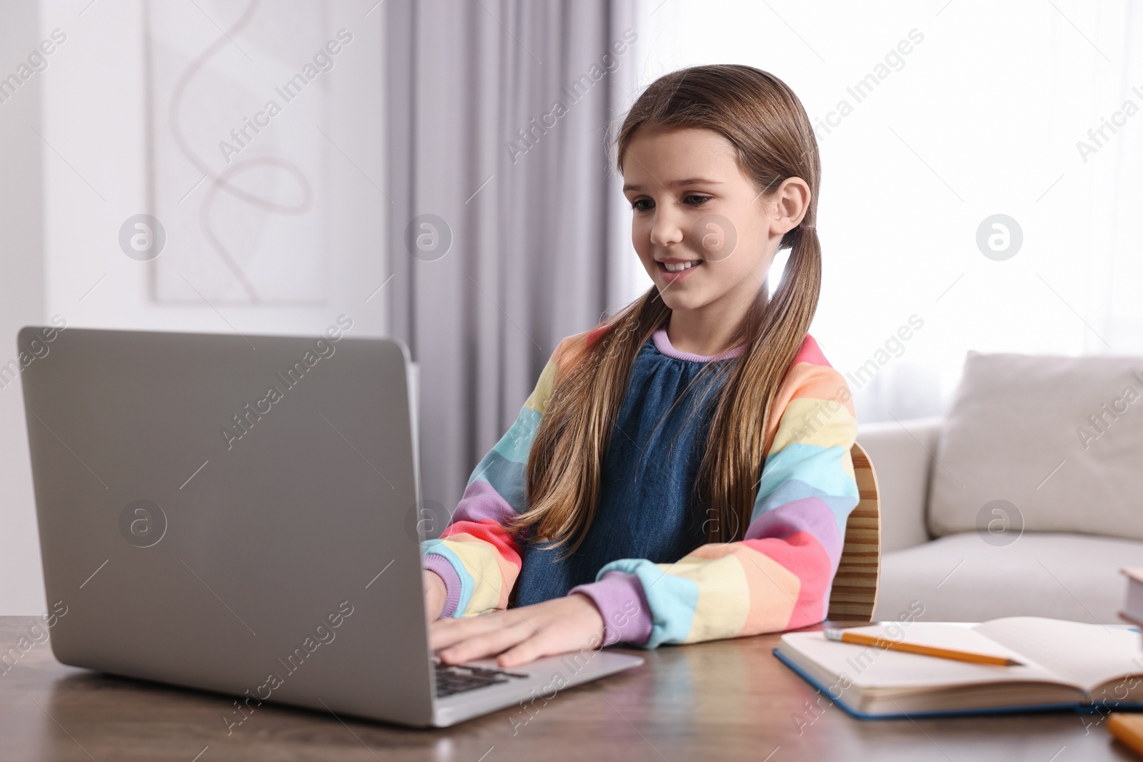 Photo of E-learning. Cute girl using laptop during online lesson at table indoors