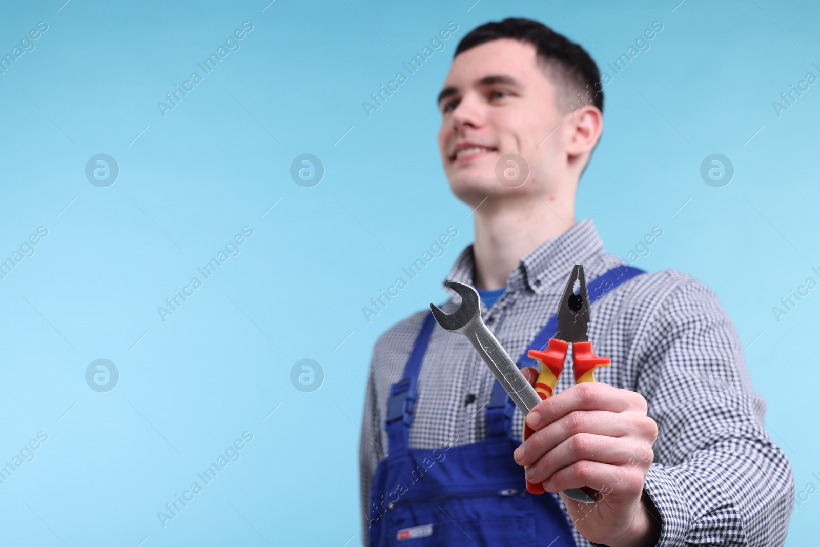 Photo of Young man holding pliers on light blue background, selective focus. Space for text