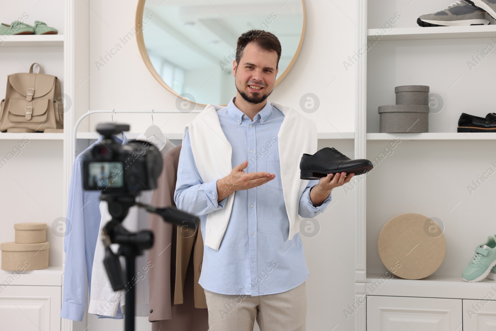 Photo of Smiling fashion blogger showing shoe while recording video at home