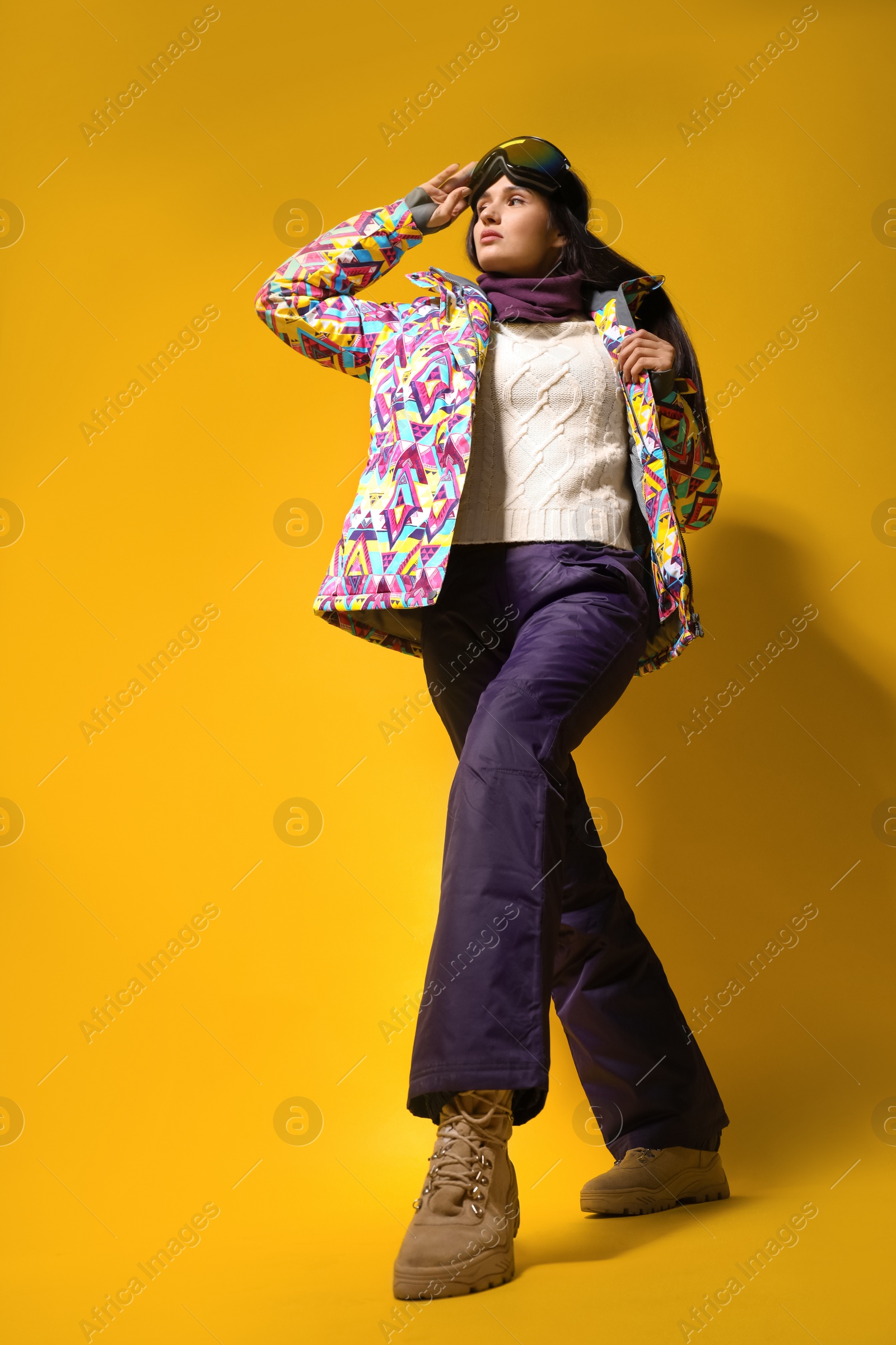 Photo of Woman wearing stylish winter sport clothes on yellow background, low angle view