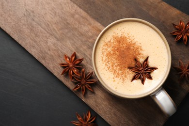 Photo of Delicious eggnog with anise and cinnamon on black table, flat lay. Space for text