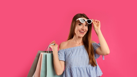Beautiful young woman with paper shopping bags on pink background