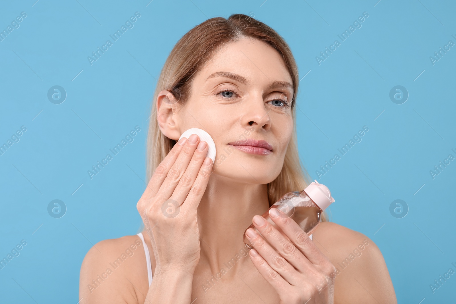 Photo of Beautiful woman removing makeup with cotton pad on light blue background