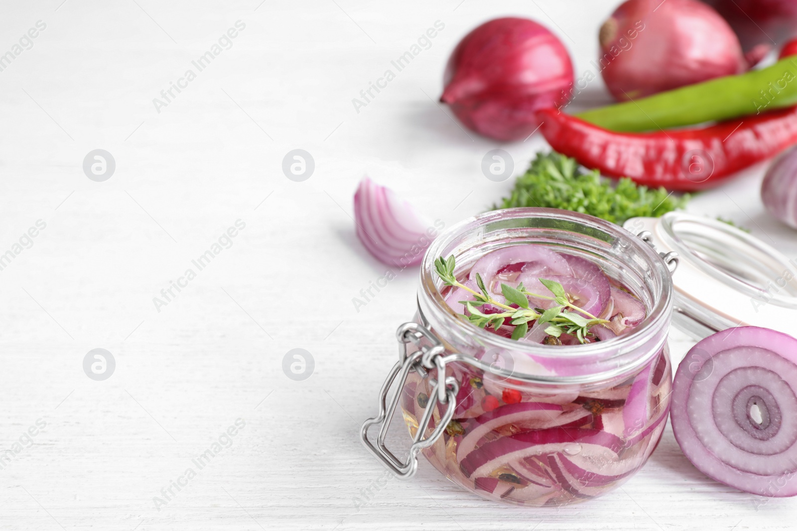 Photo of Jar with pickled onions on white wooden table. Space for text