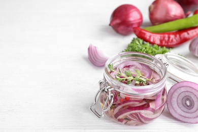 Photo of Jar with pickled onions on white wooden table. Space for text