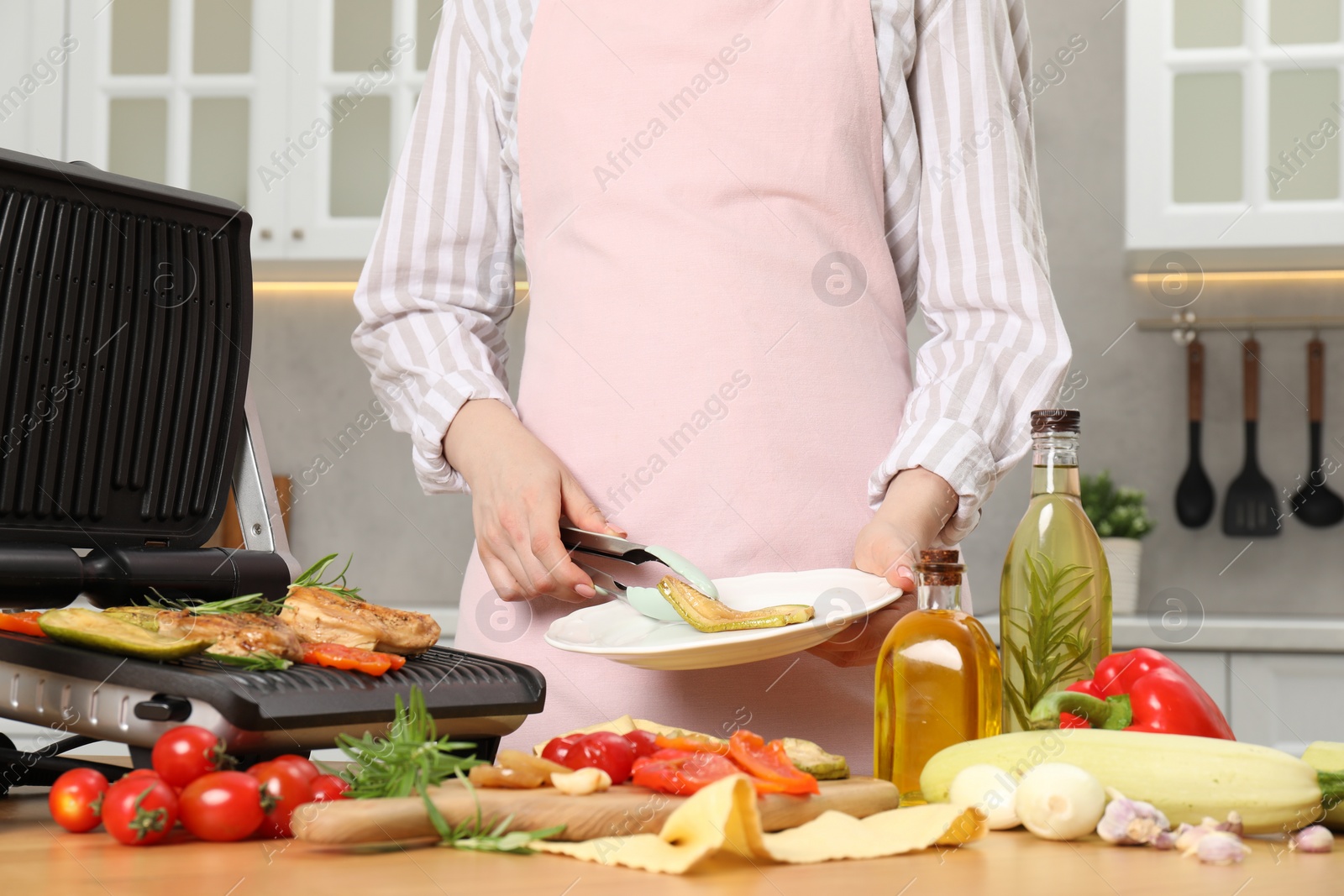 Photo of Woman cooking different products with electric grill at wooden table in kitchen, closeup