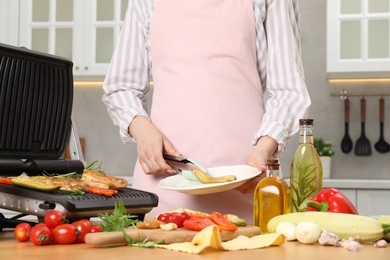 Woman cooking different products with electric grill at wooden table in kitchen, closeup