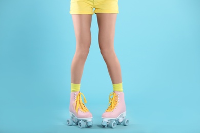 Young woman with retro roller skates on color background, closeup