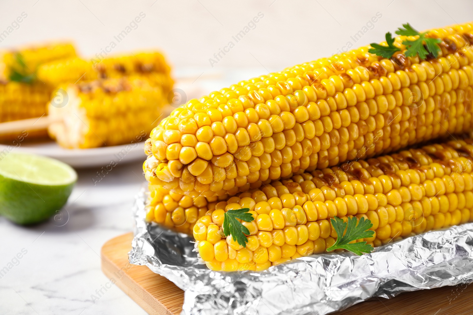 Photo of Tasty grilled corn on wooden board, closeup