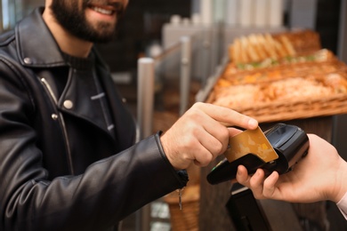 Man with credit card using payment terminal at shop, closeup