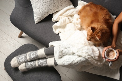 Photo of Woman with cute red cat and coffee on grey sofa at home, top view