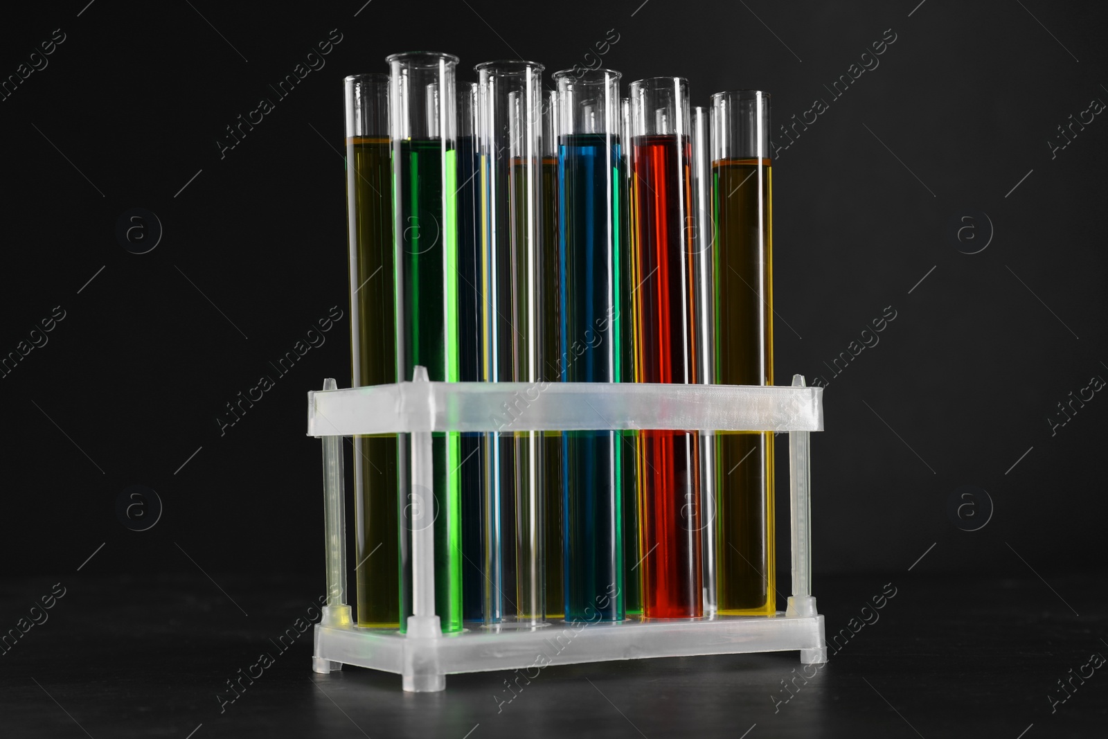 Photo of Many test tubes with liquids in stand on black background