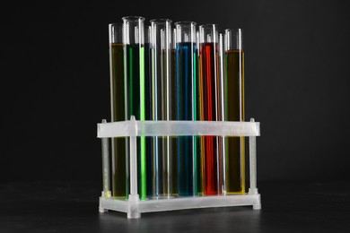 Photo of Many test tubes with liquids in stand on black background