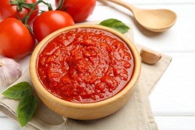 Photo of Homemade tomato sauce in bowl, spoon and fresh ingredients on white wooden table, closeup