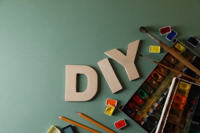 Photo of Abbreviation DIY made of letters and different painting supplies on pale green background, flat lay. Space for text