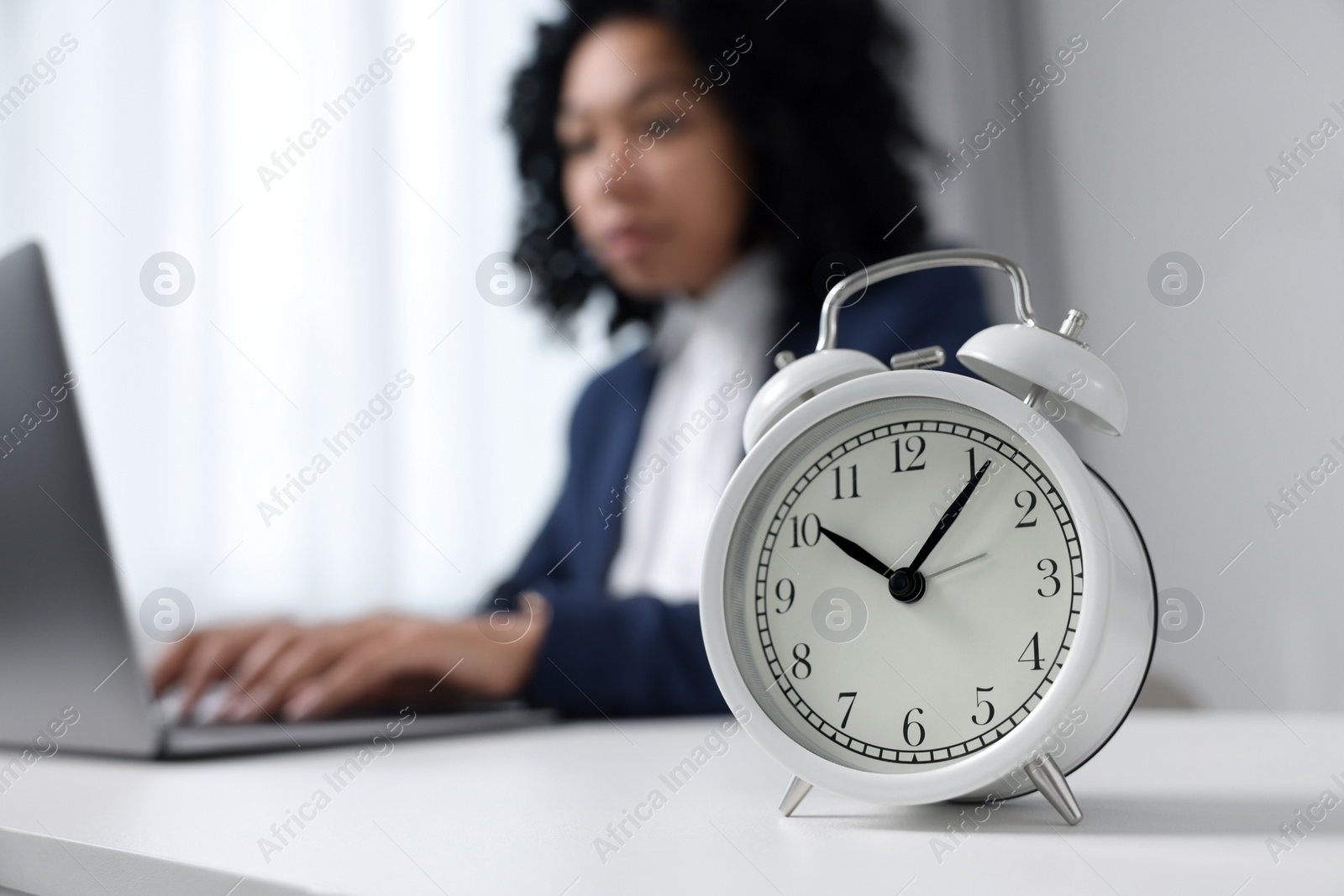 Photo of Stressful deadline. Alarm clock near woman working at white desk indoors, selective focus. Space for text