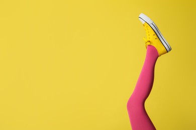 Woman wearing pink tights and sport shoes on yellow background, closeup. Space for text