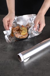 Photo of Aluminum foil and woman with tasty salmon at grey textured table, closeup