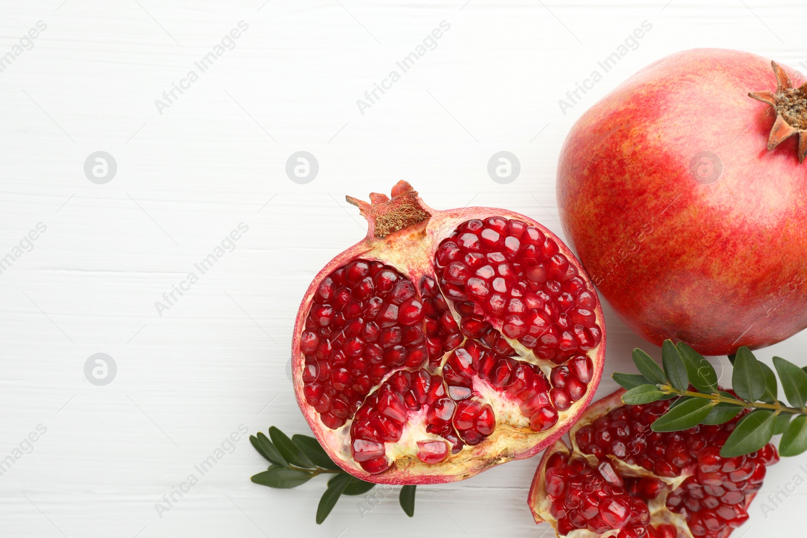 Photo of Fresh pomegranates and branches on white wooden table, flat lay. Space for text