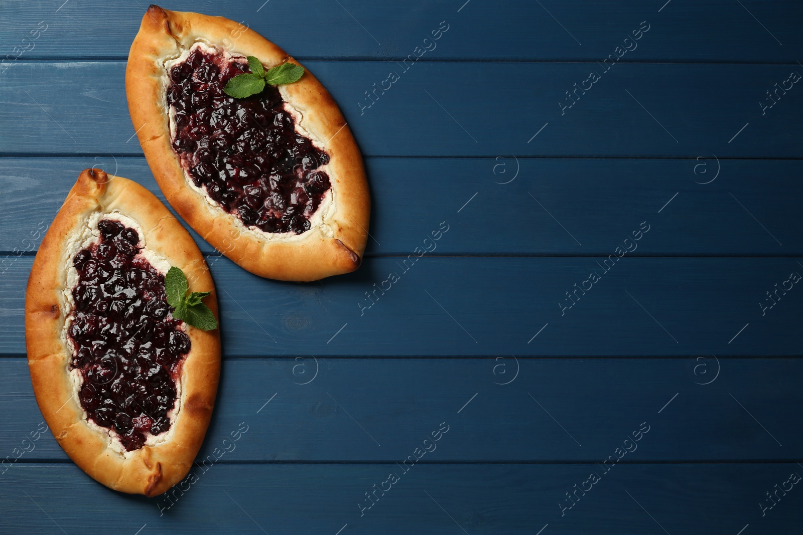 Photo of Delicious sweet cottage cheese pastry with cherry jam on blue wooden table, flat lay. Space for text