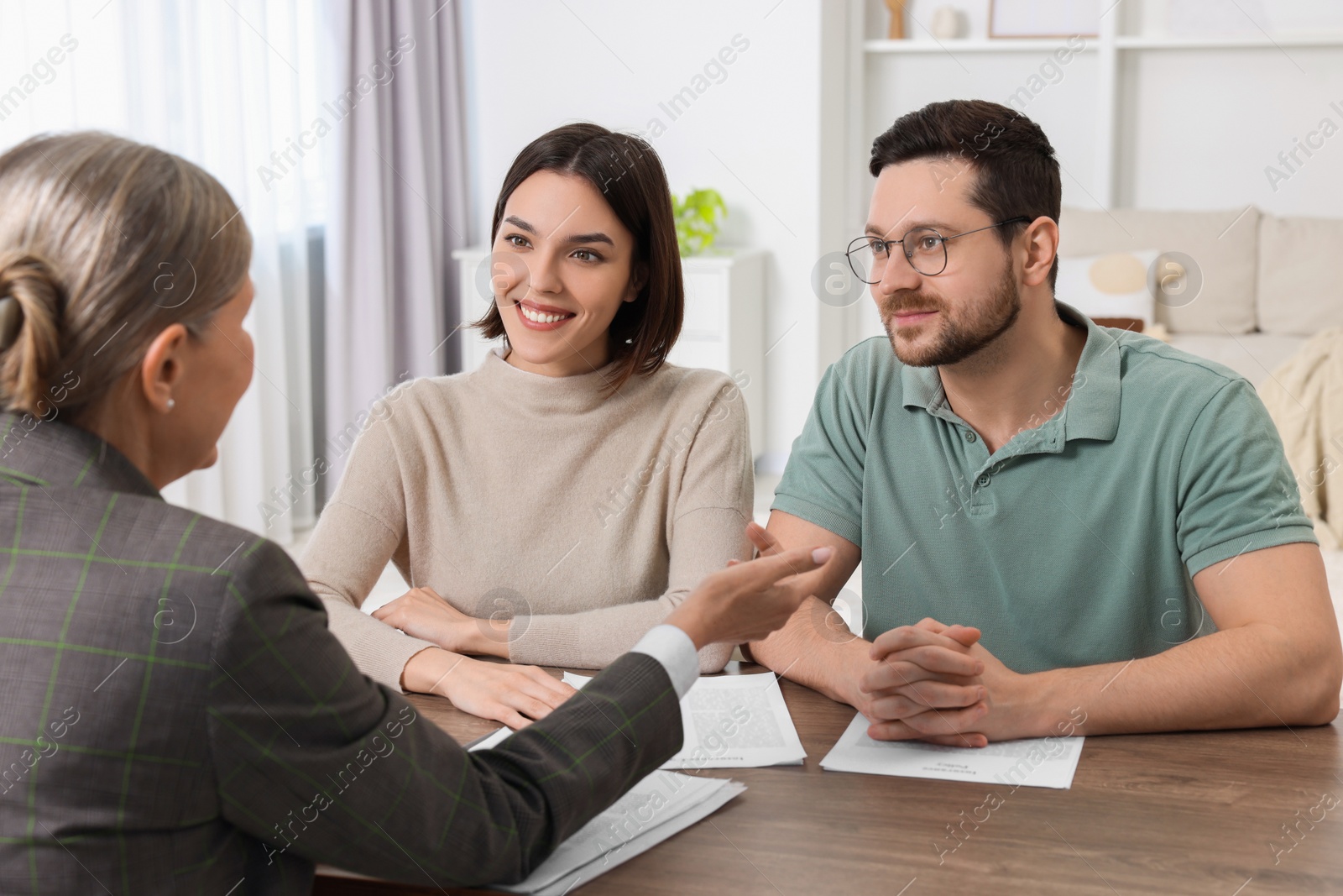 Photo of Young couple consulting insurance agent about pension plan at wooden table indoors