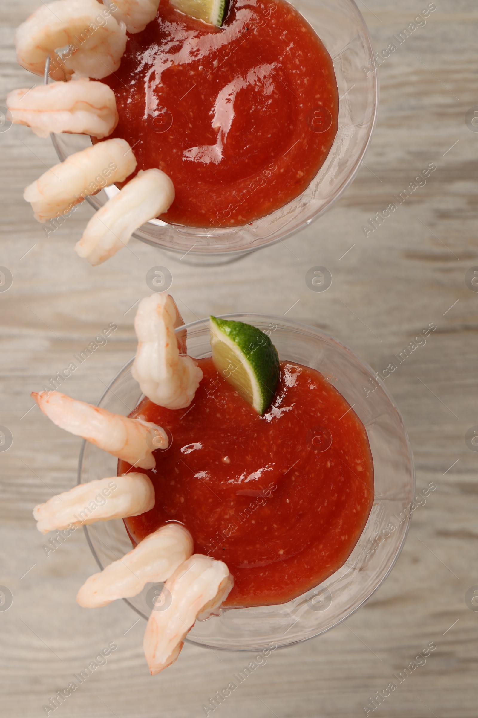 Photo of Tasty shrimp cocktail with sauce and lime in glasses on wooden table, flat lay